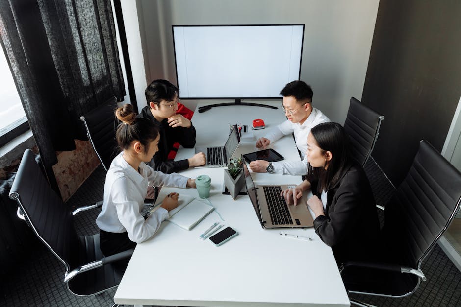Four professionals collaborating over laptops in a bright, modern office space